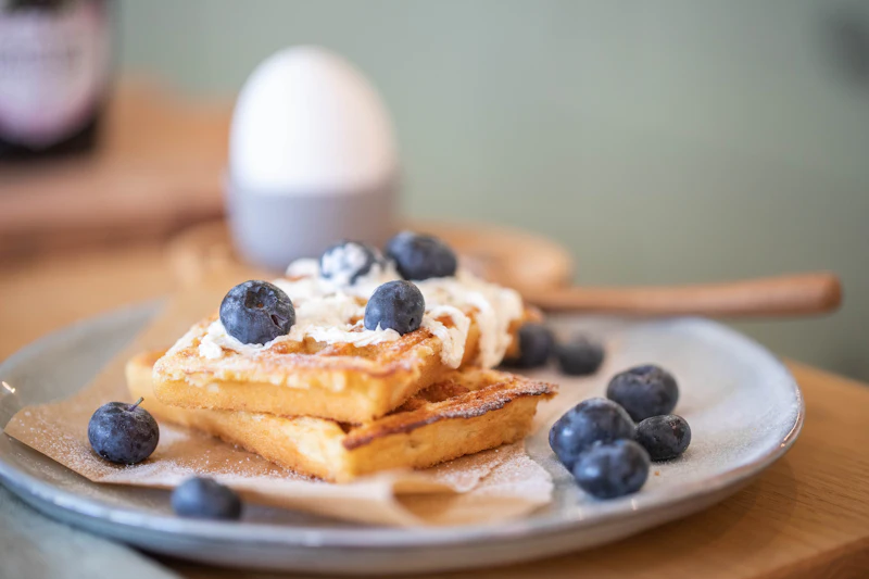 Buttermilk waffles topped with whipped cream and fresh blueberries on a grey stoneware plate.