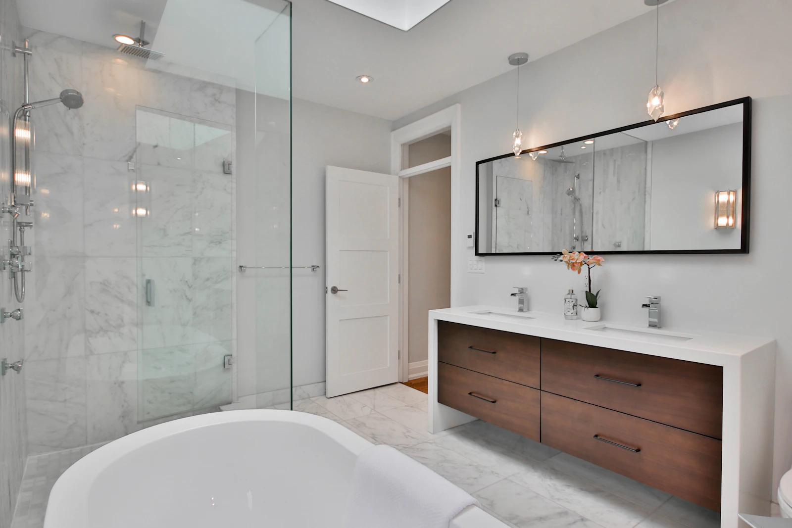 Marble-tiled bathroom with a frameless glass shower, soaking tub and walnut double vanity
