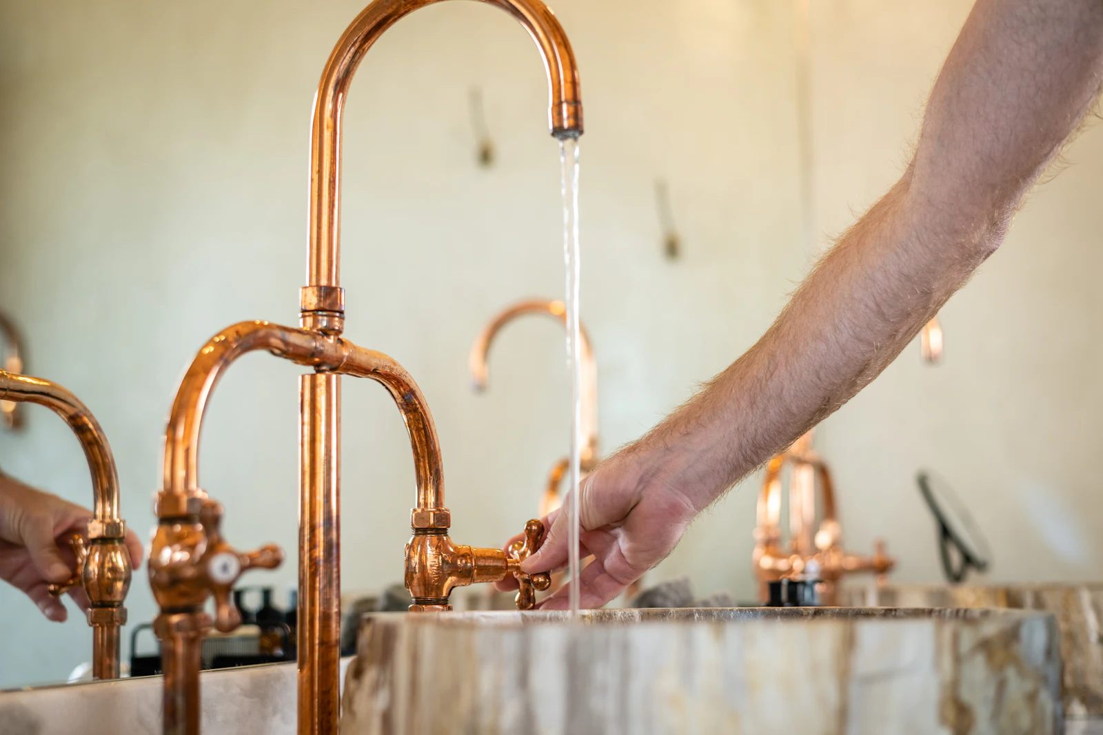 A hand turns on a polished copper tap above a stone basin