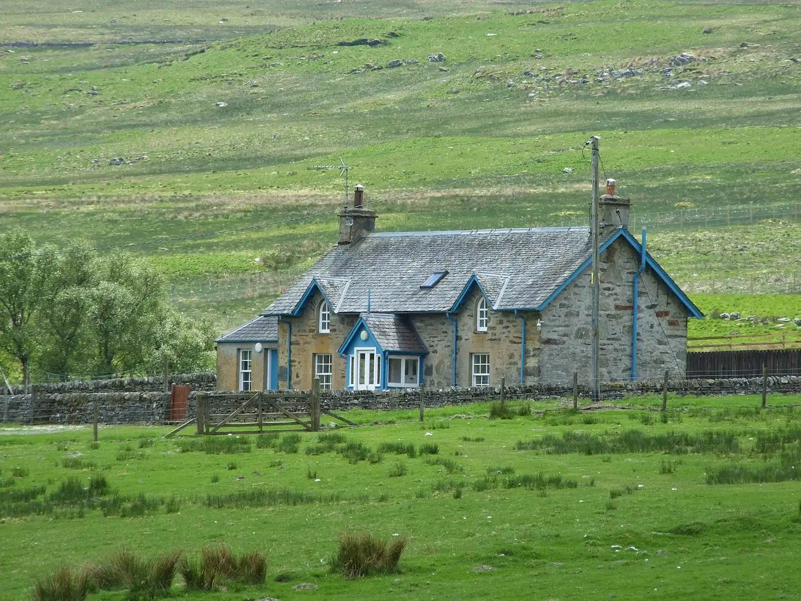 A sandstone farmhouse with blue-painted gables and a slate roof in open green hill country
