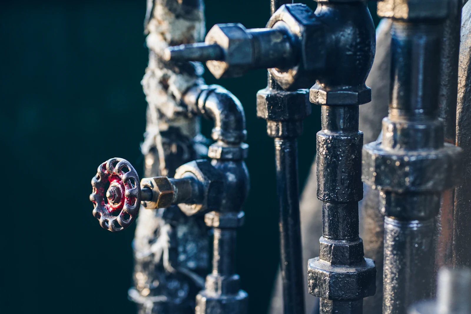 Close-up of black iron pipework with a red stop-valve wheel