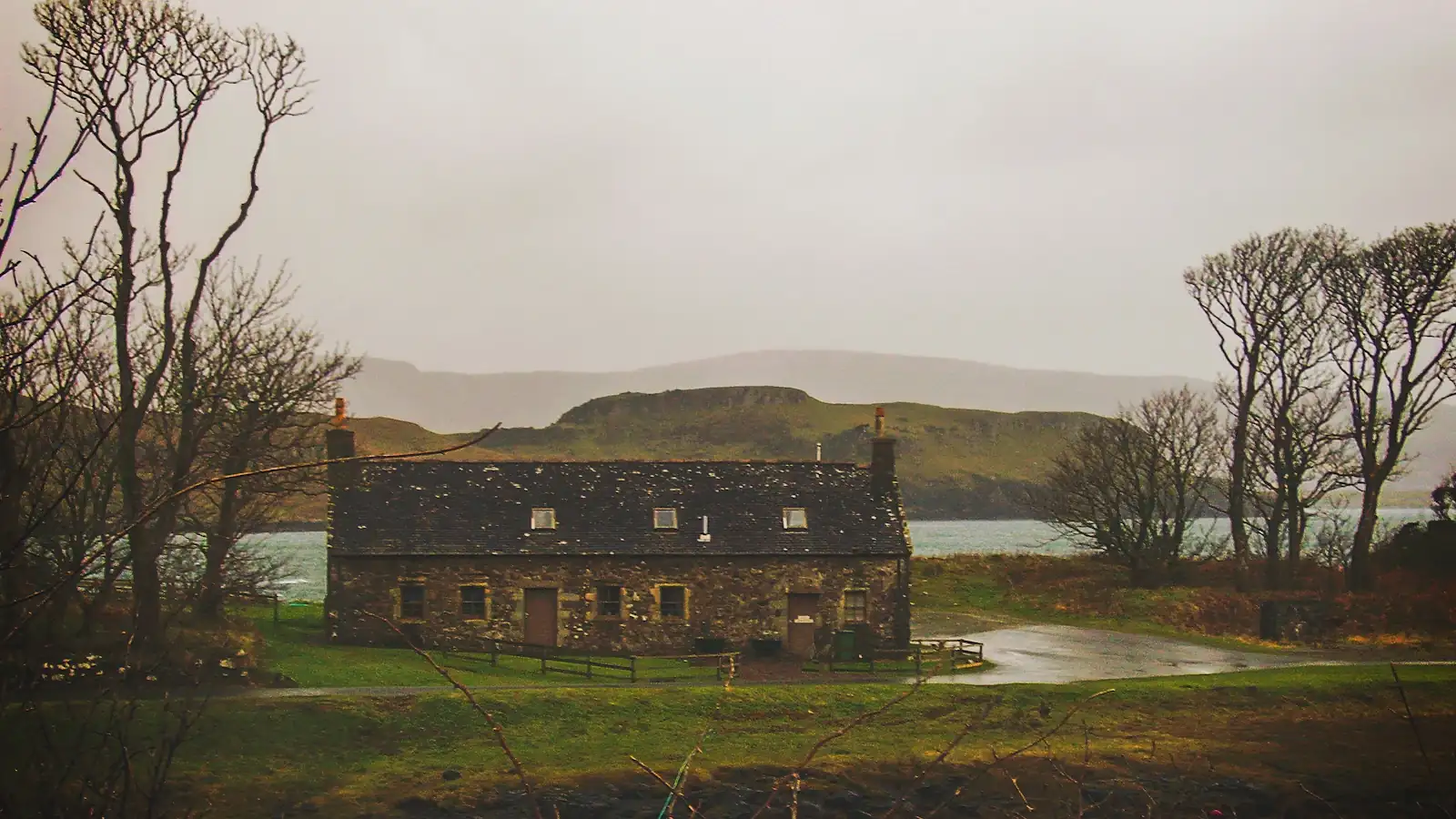 A stone farmhouse beneath low grey cloud and bare winter trees